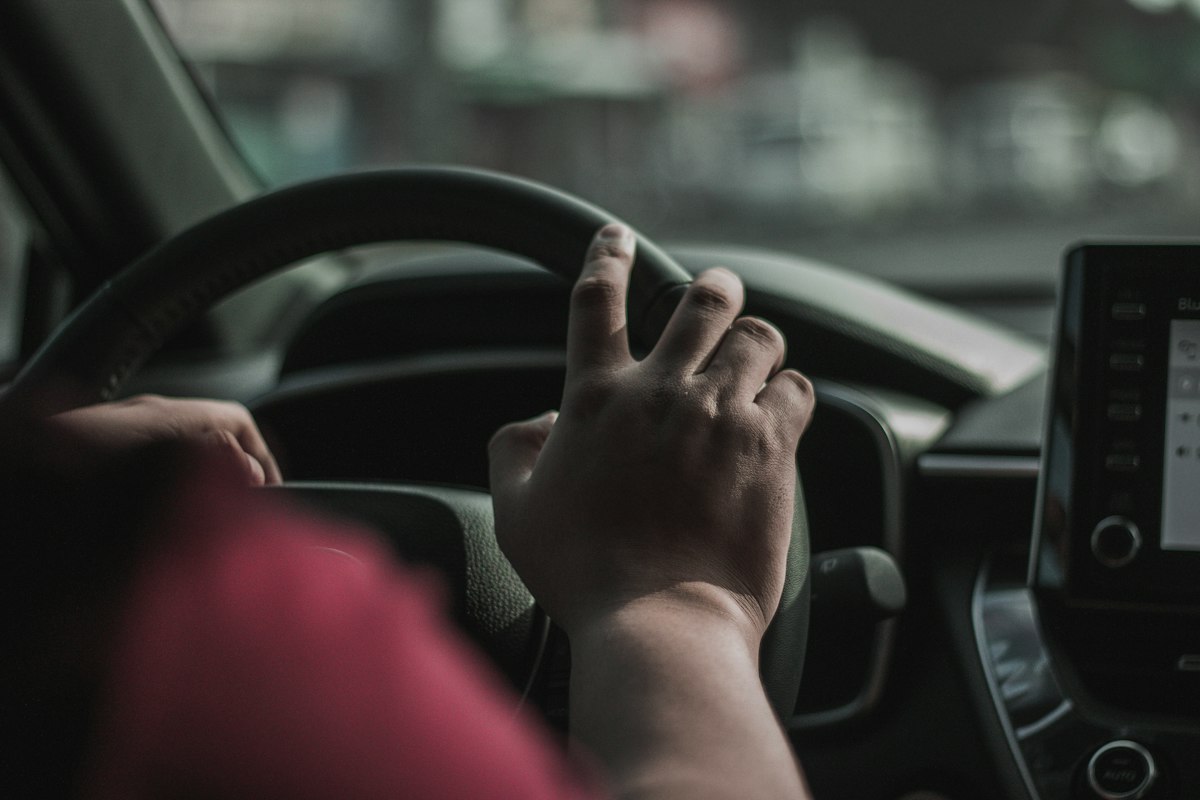 Main d'un conducteur posée sur le volant d'une voiture, vue depuis le siège conducteur