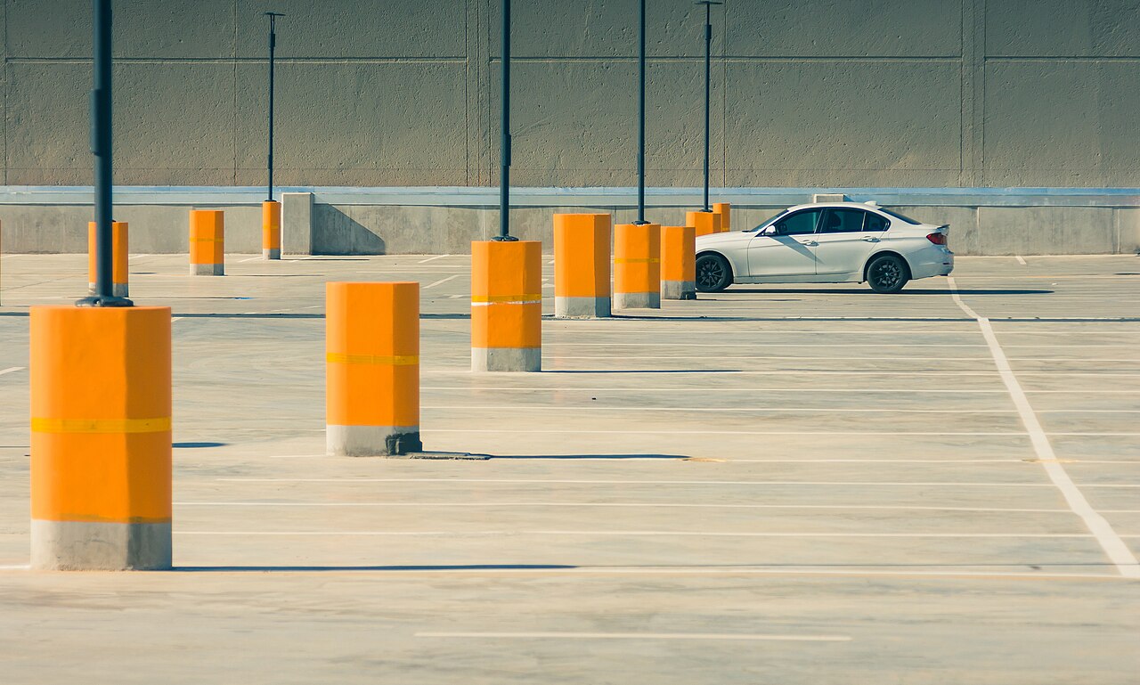Berline blanche récente stationnée seule sur un parking en béton bordé de poteaux orange