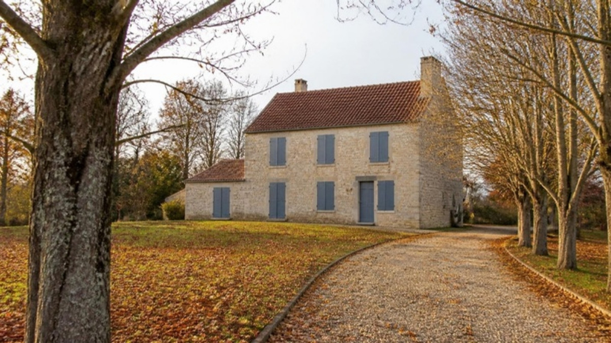 Maison de campagne aux volets fermés en fin d’automne, allée bordée d’arbres