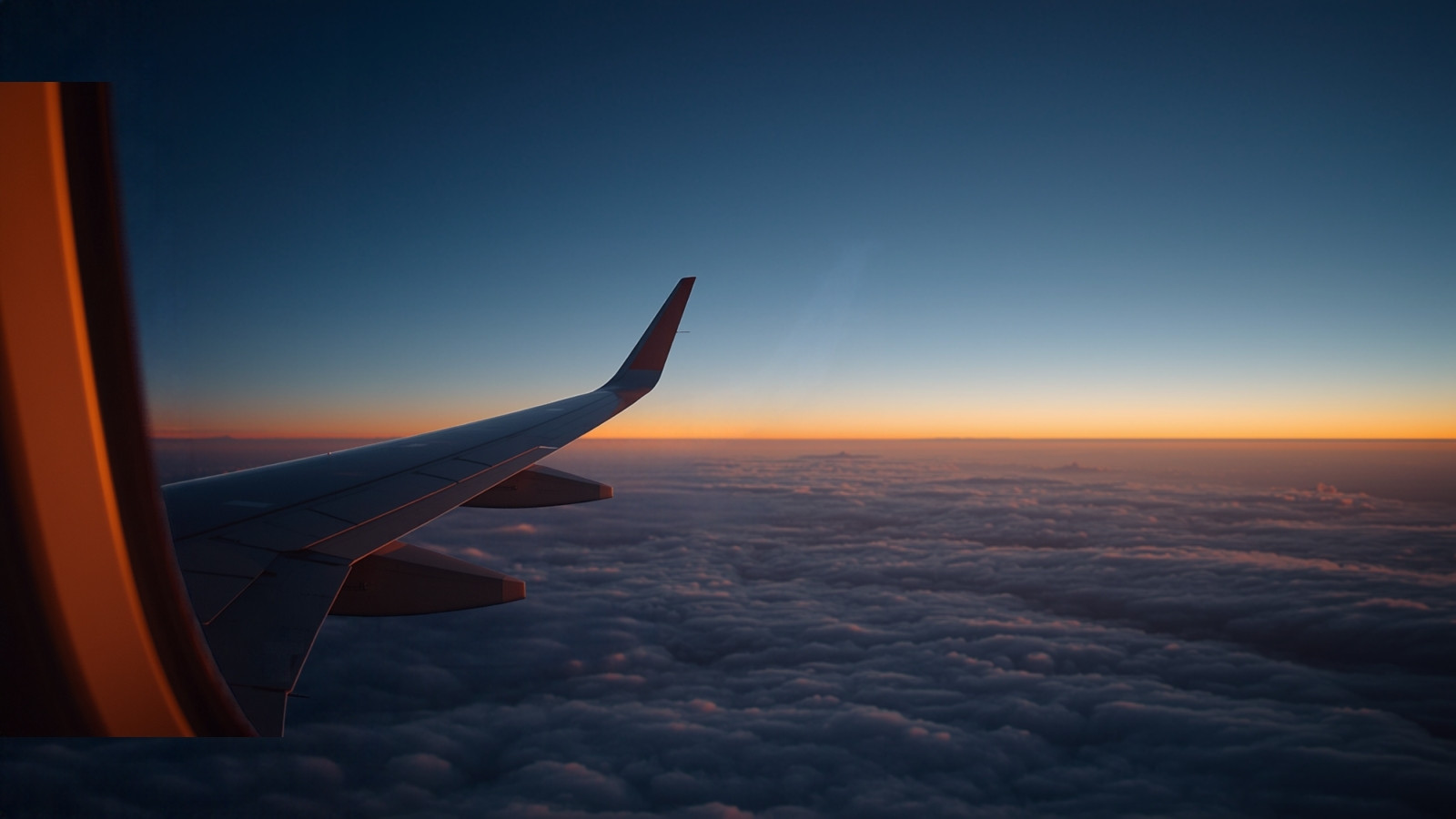 Vue d’une aile d’avion au-dessus des nuages au coucher du soleil, hublot de cabine