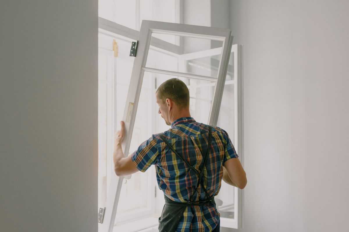 Artisan installant une fenêtre neuve dans une pièce en cours de rénovation, ancien dormant déposé
