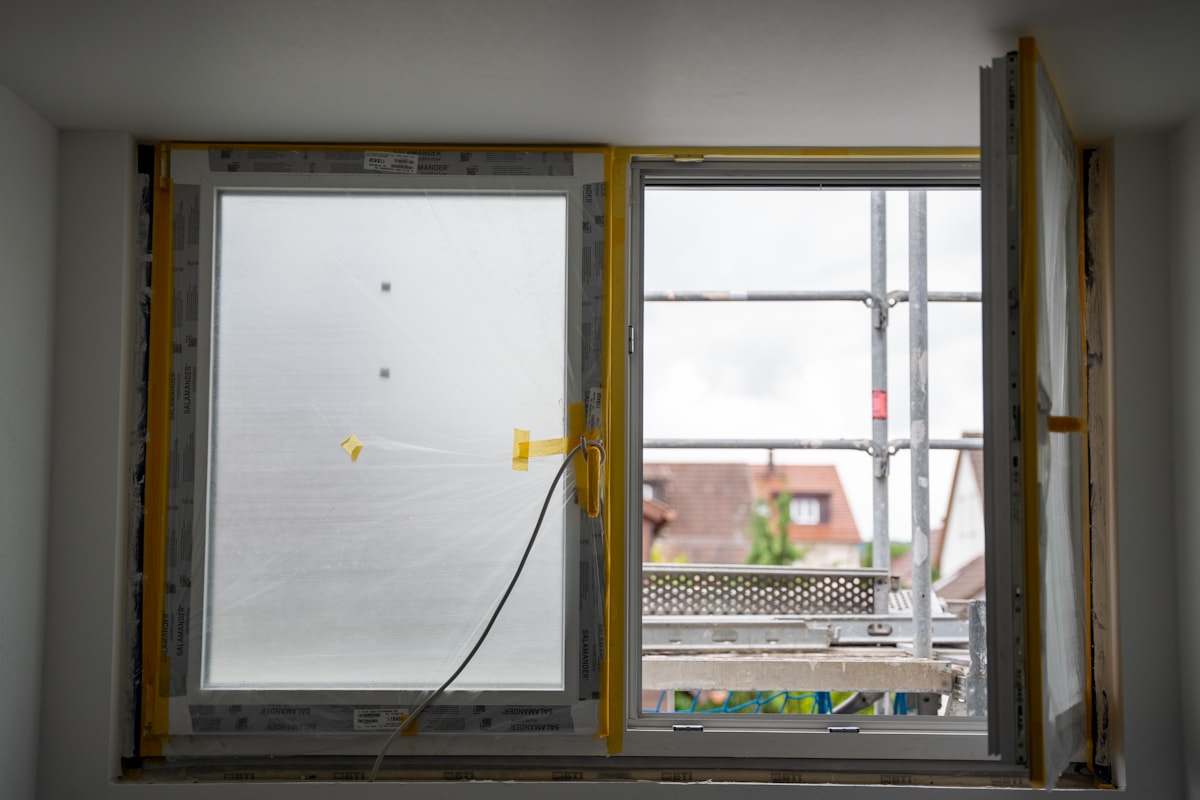 Fenêtre ouverte sur un chantier de façade en cours, vue depuis l'intérieur d'un logement en rénovation