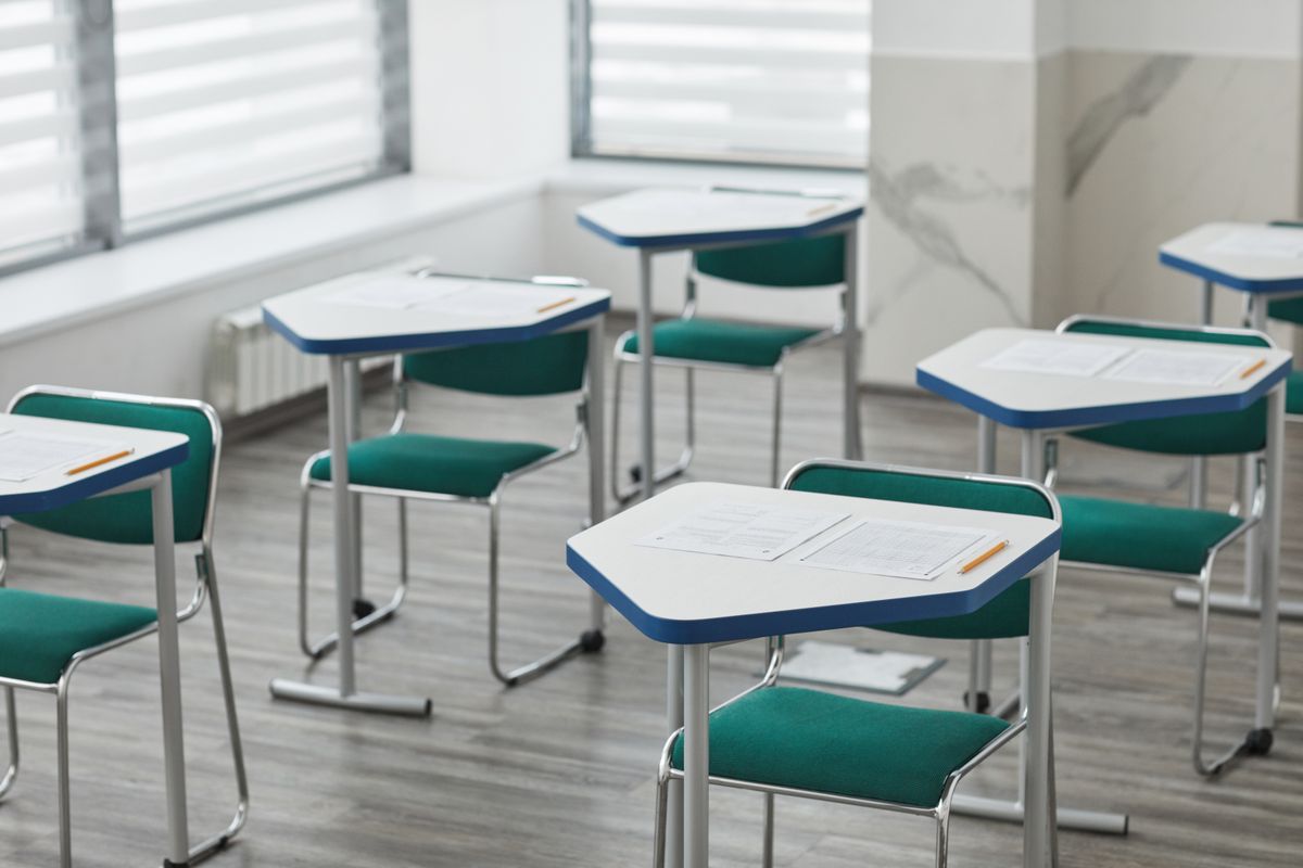 Salle de classe vide avec pupitres, feuilles et crayons posés sur les tables