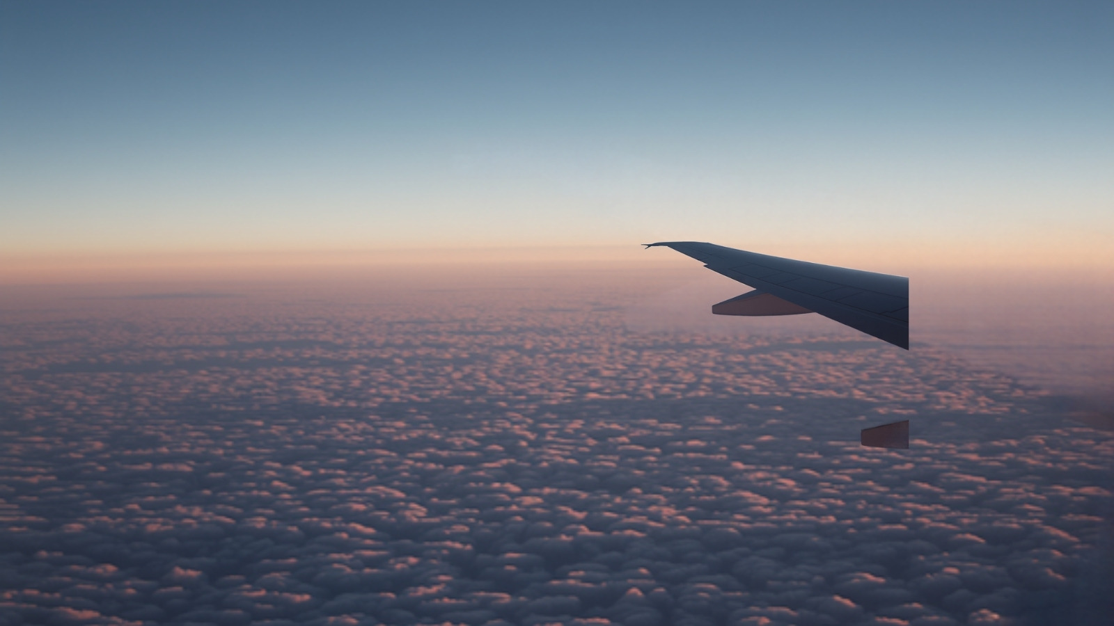 Aile d’un avion de ligne au-dessus d’une mer de nuages au lever du jour, vue depuis un hublot.