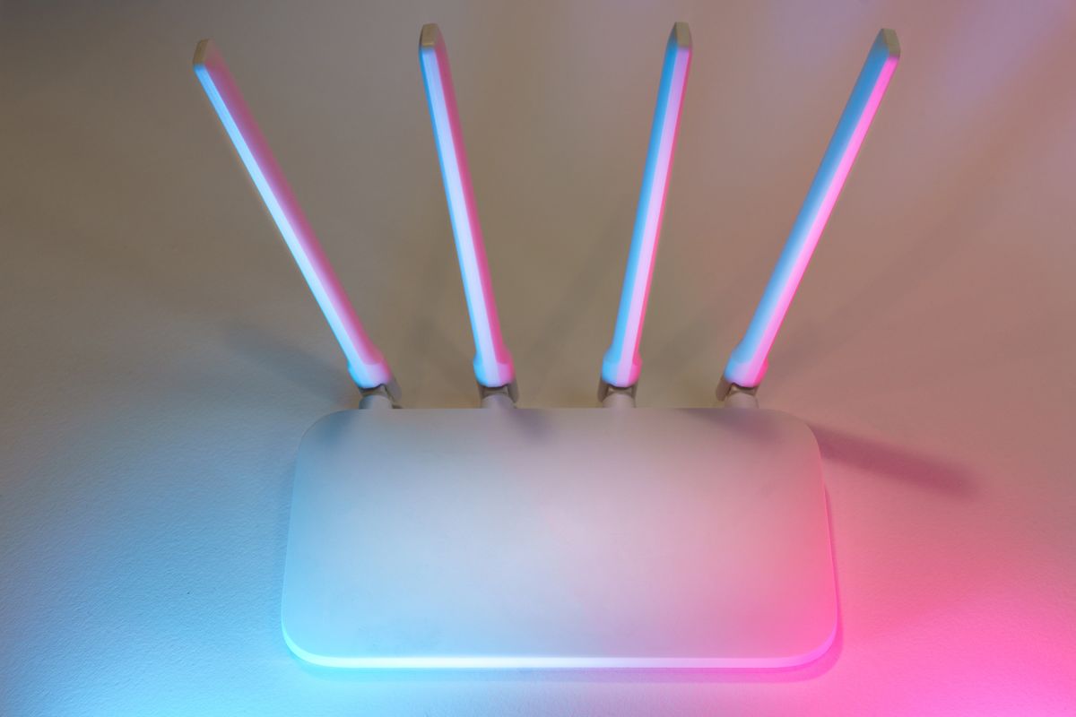 Routeur Wi-Fi domestique posé contre un mur clair, ses quatre antennes dressées, éclairé en bleu et rose
