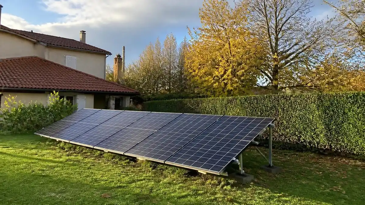 Rangée de panneaux photovoltaïques montés sur une structure métallique posée au sol dans le jardin d'une maison individuelle, en fin d'après-midi d'automne