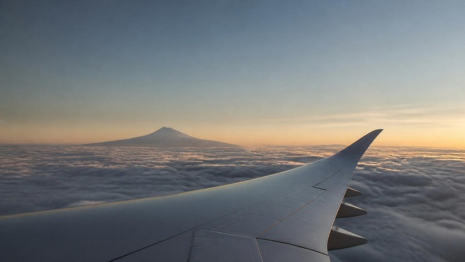Aile d’un avion de ligne au-dessus d’une mer de nuages, avec un relief montagneux japonais à l’horizon dans la lumière du matin.