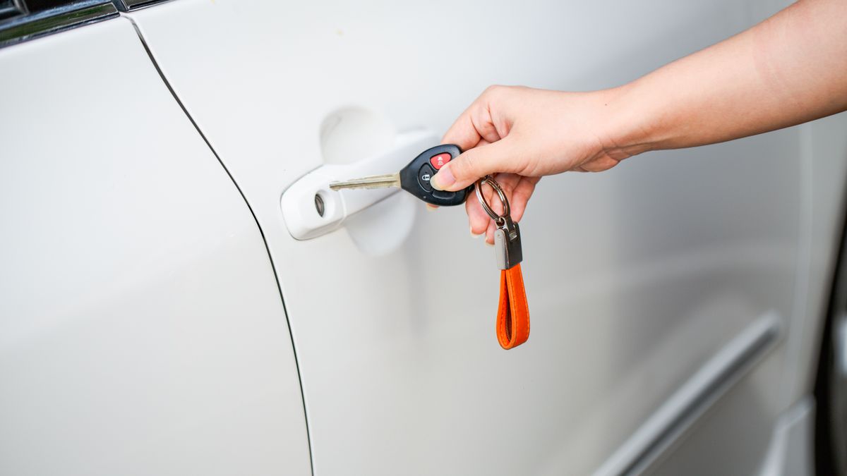 Main tenant une clé de voiture devant la poignée de portière d'un véhicule blanc